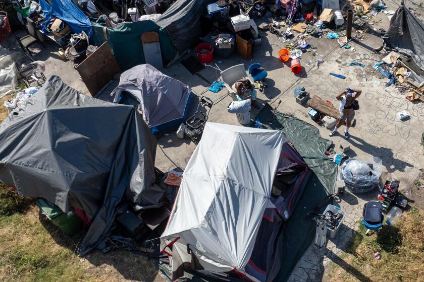 Los Angeles, CA - June 26: A homeless woman waits as Inside Safe workers canvas a homeless camp on 86th and Broadway to move people out of the encampment and into hotel and motel rooms Wednesday, June 26, 2024 in Los Angeles, CA. (Brian van der Brug / Los Angeles Times)