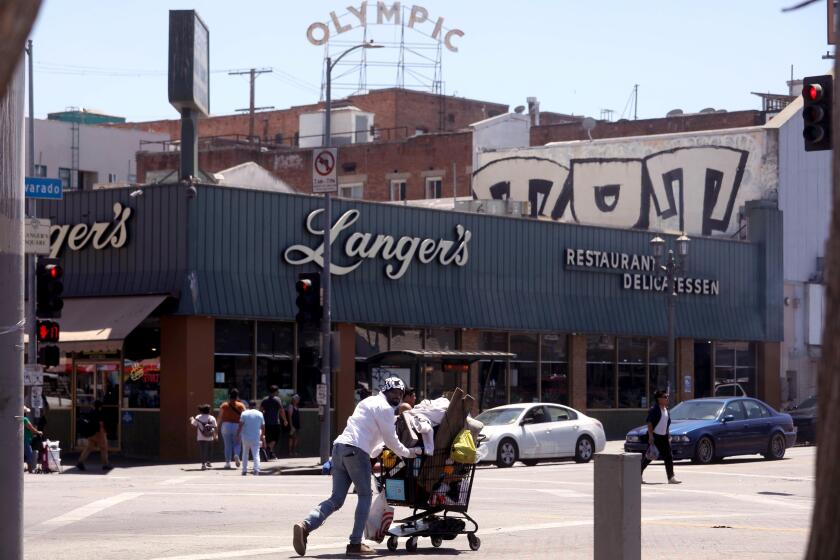 LOS ANGELES, CA - AUGUST 21, 2024 - A man walks with his belongings in a shopping cart across the street from Langer's Deli, also known as Langer's Delicatessen-Restaurant, in in the Westlake neighborhood of Los Angeles, opposite MacArthur Park, on August 21, 2024. Norm Langer, 79, president and chief executive of Langer's Delicatessen-Restaurant, is thinking of closing the deli after 77 years in business, due to neighborhood challenges. (Genaro Molina/Los Angeles Times)