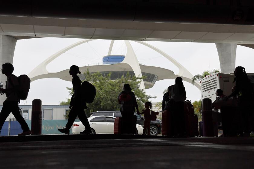 Los Angeles, CA - August 29: Travelers are silhouetted by The Theme Building as they arrive and find transportation while kicking off the getaway Labor Day weekend travel at LAX in Los Angeles Thursday, Aug. 29, 2024. (Allen J. Schaben / Los Angeles Times)