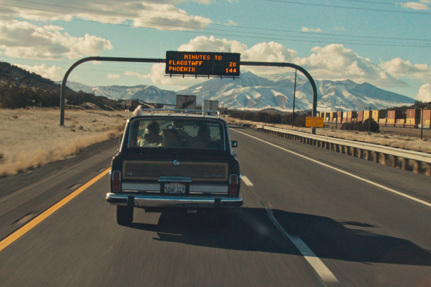 A Jeep Wagoneer on the freeway passes under a sign indicating times to Flagstaff and Phoenix.