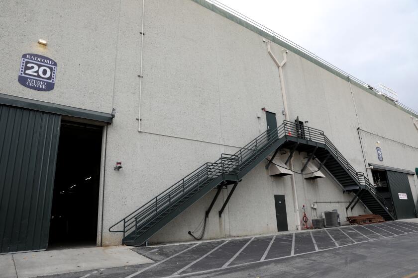 The gray exterior of a soundstage building with green fire-escape staircases on the side