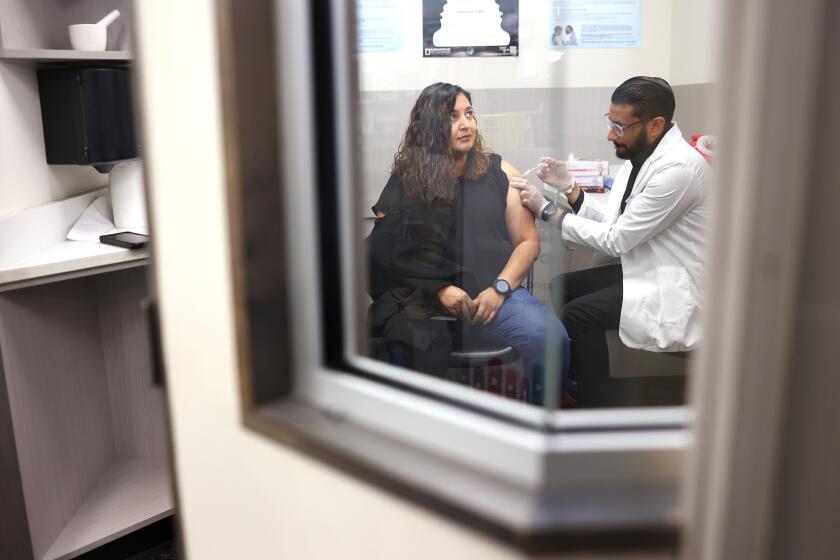 HUNTINGTON PARK-CA-AUGUST 28, 2024: Cynthia Blancas, 42, of Lynwood, receives a Covid-19 vaccine by pharmacist Deep Patel, right, at CVS in Huntington Park on August 28, 2024. (Christina House / Los Angeles Times)