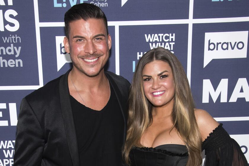 Jax Taylor standing in a black jacket over a black T-shirt with his arm around Brittany Cartwright in a strapless black dress